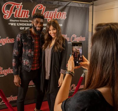 a couple getting their photo taken in front of Film Clayton poster